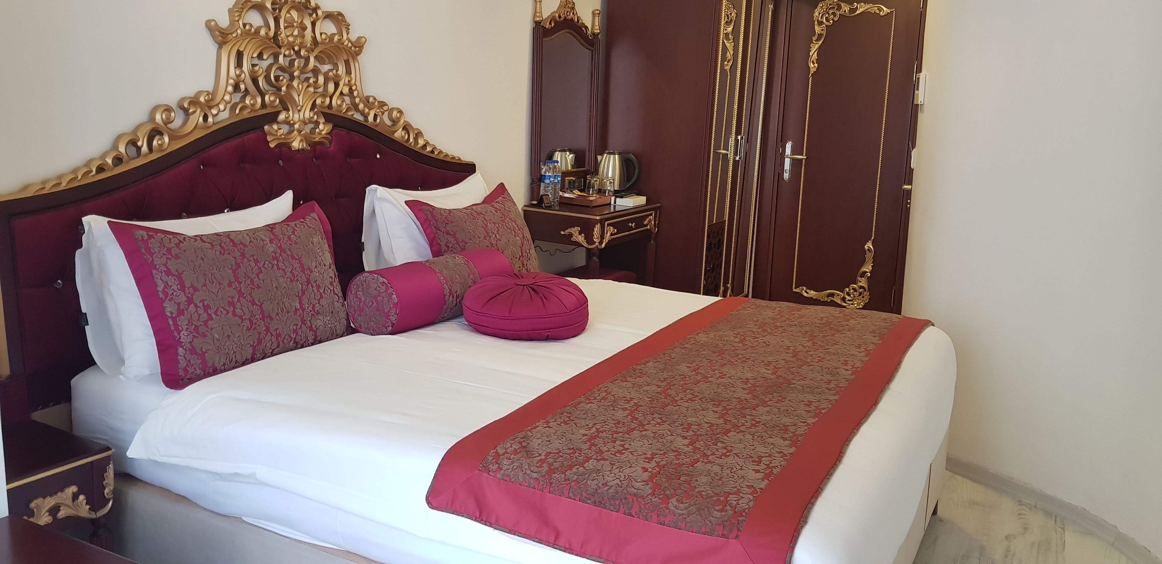 Ein Hotelzimmer mit einem großen Bett, einem verzierten Kopfteil und einem Schrank mit Spiegel.