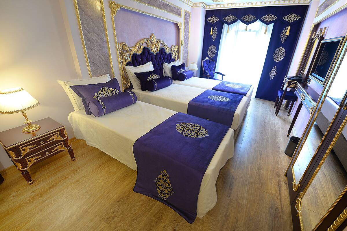 A hotel room with two beds, a nightstand, a lamp, and a large mirror.