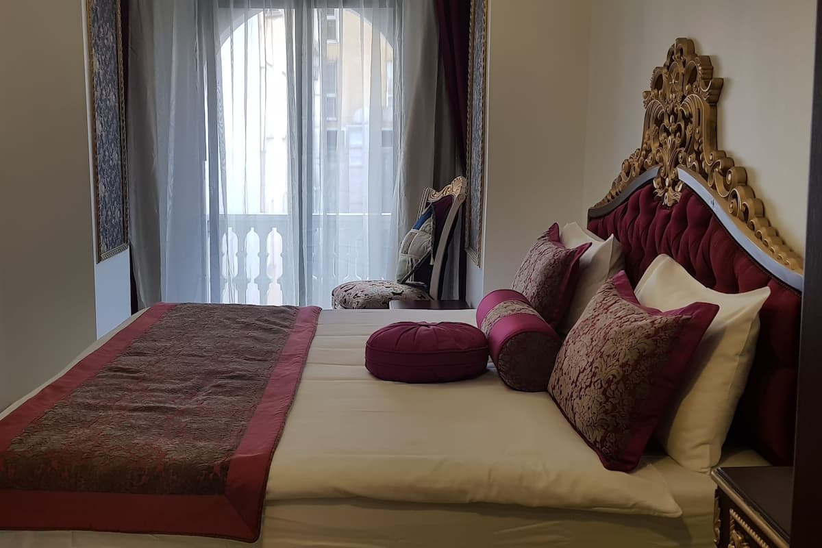 A bedroom with a four-poster bed, a large window with curtains, and a television mounted on the wall.