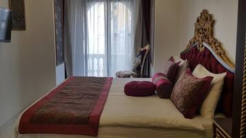 Ein Schlafzimmer mit einem Himmelbett, einem großen Fenster mit Vorhängen und einem an der Wand befestigten Fernseher.