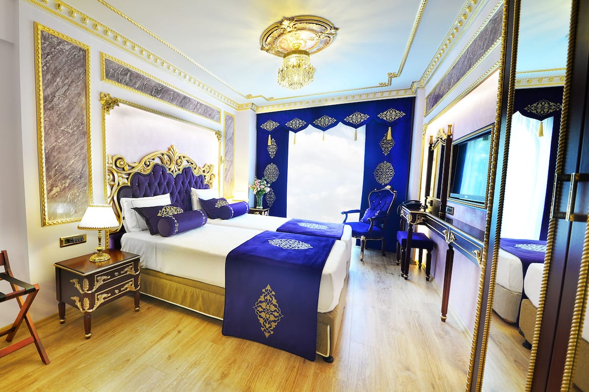 A luxurious bedroom with a large bed, ornate headboard, a chandelier, and a mirror.