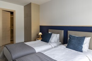Una habitación de hotel con dos camas, un armario y una mesita de noche con lámpara.