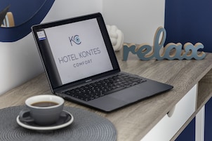 Un ordinateur portable sur un bureau en bois, une tasse de café, une pancarte indiquant « HÔTEL KONTES COMFORT » et un mot décoratif : « détente ».