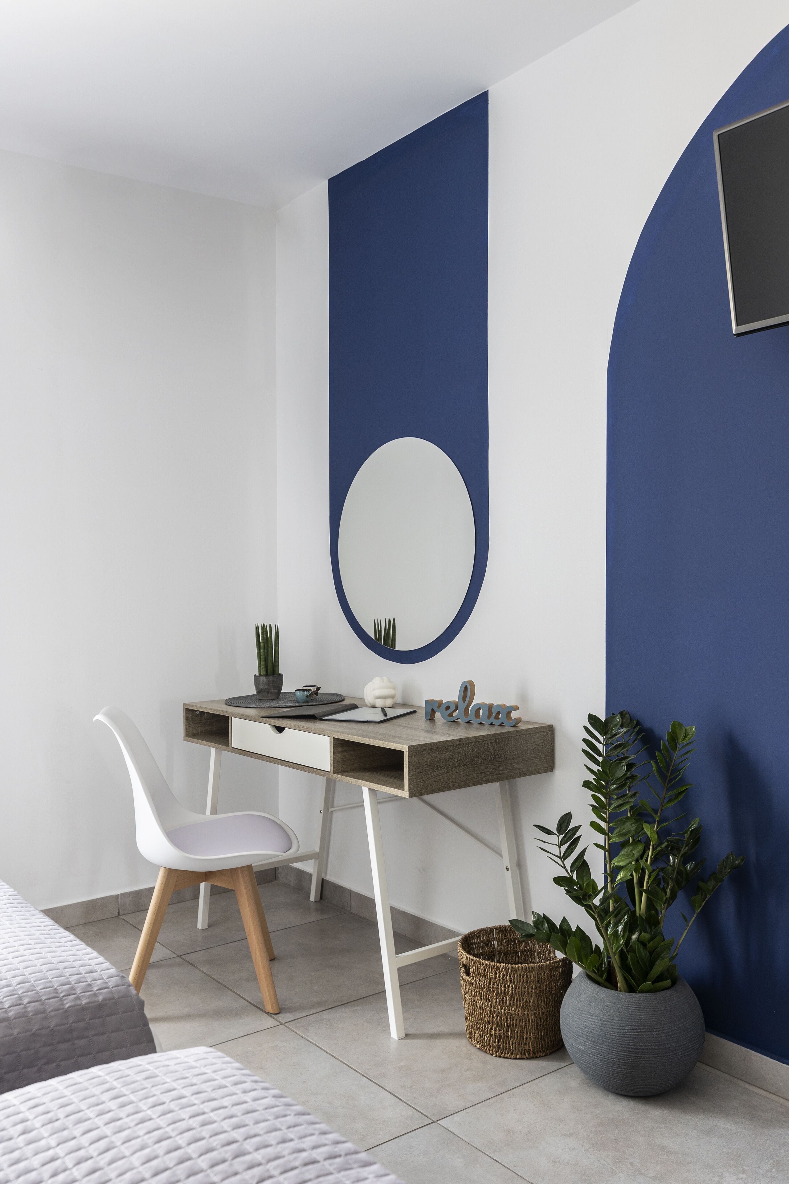 A modern bedroom with a desk, a white chair, a potted plant, and a bed.