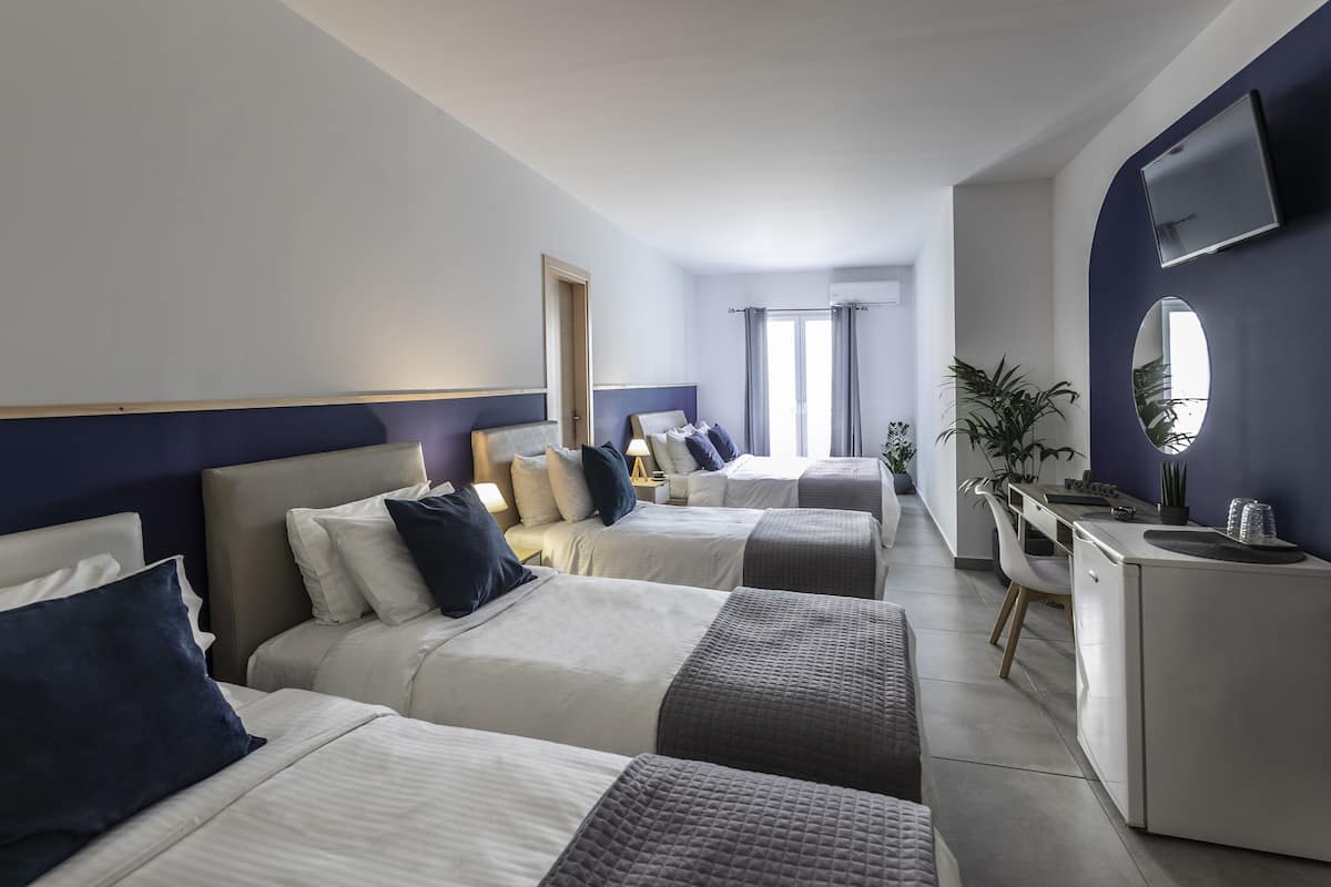 Habitación de hotel con tres camas, un escritorio, un espejo y una planta en maceta.