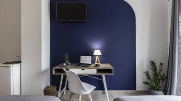 A hotel room with a desk, a laptop, a lamp, a potted plant, and two beds.