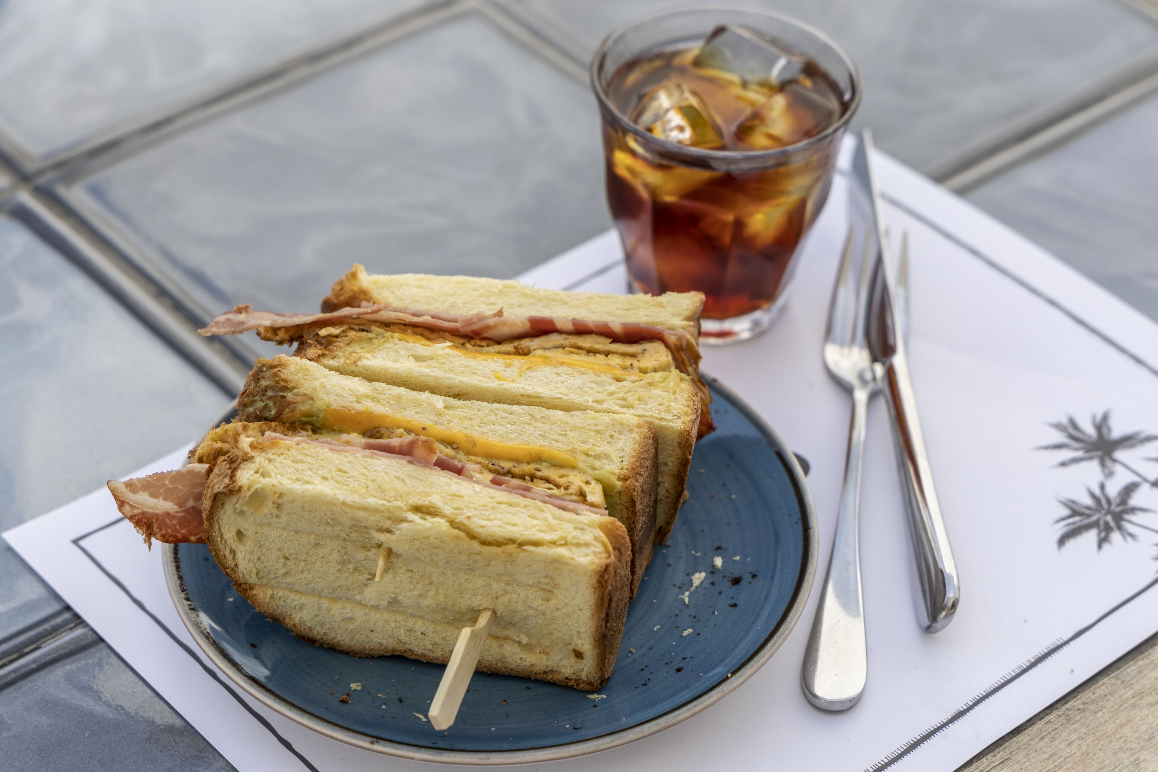 A sandwich on a plate with a glass of iced tea and a fork.
