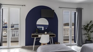 Quarto com cama, escrivaninha, cadeira, televisão e vista para o mar pelas portas de correr.