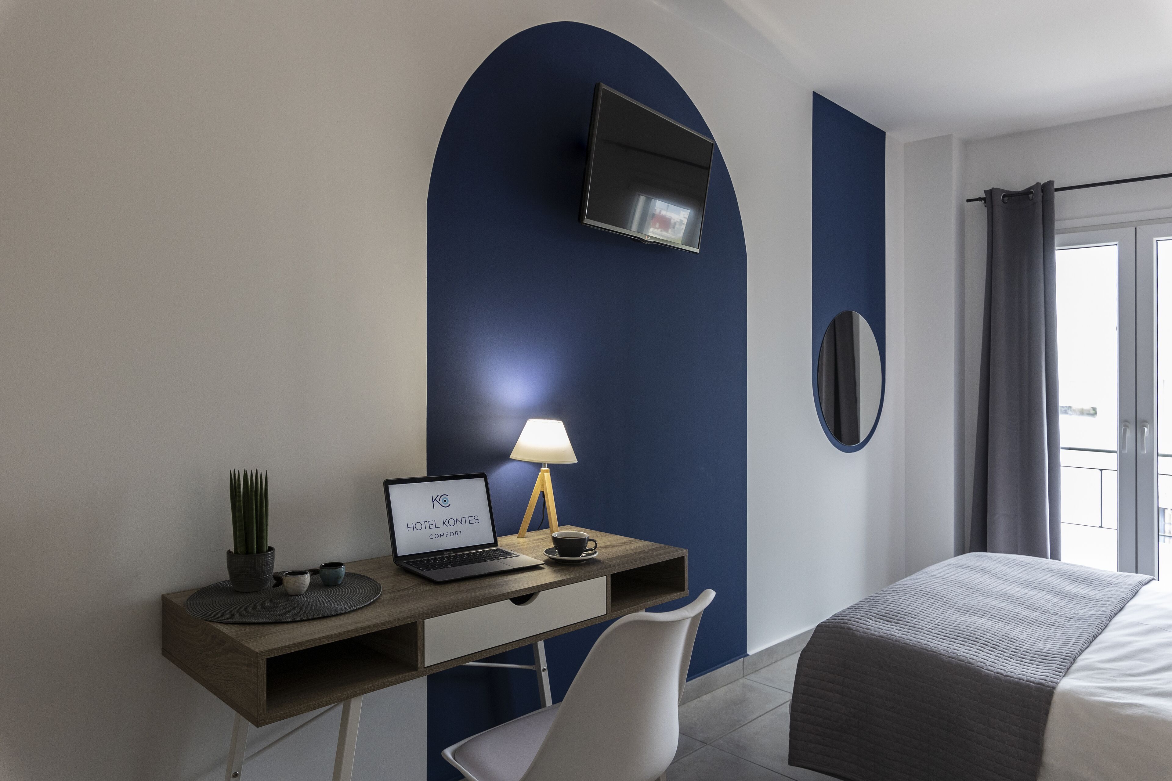 Een hotelkamer met een bureau, laptop, lamp en een bed.