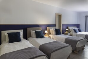 Une chambre d’hôtel avec trois lits, chacun doté d’une tête de lit, de tables de chevet et de lampes.