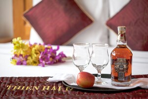 A bed with a red and gold bedspread, two glasses, a bottle of Chivas Regal, and an apple on a tray.