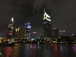 A nighttime cityscape with illuminated skyscrapers along a waterfront.