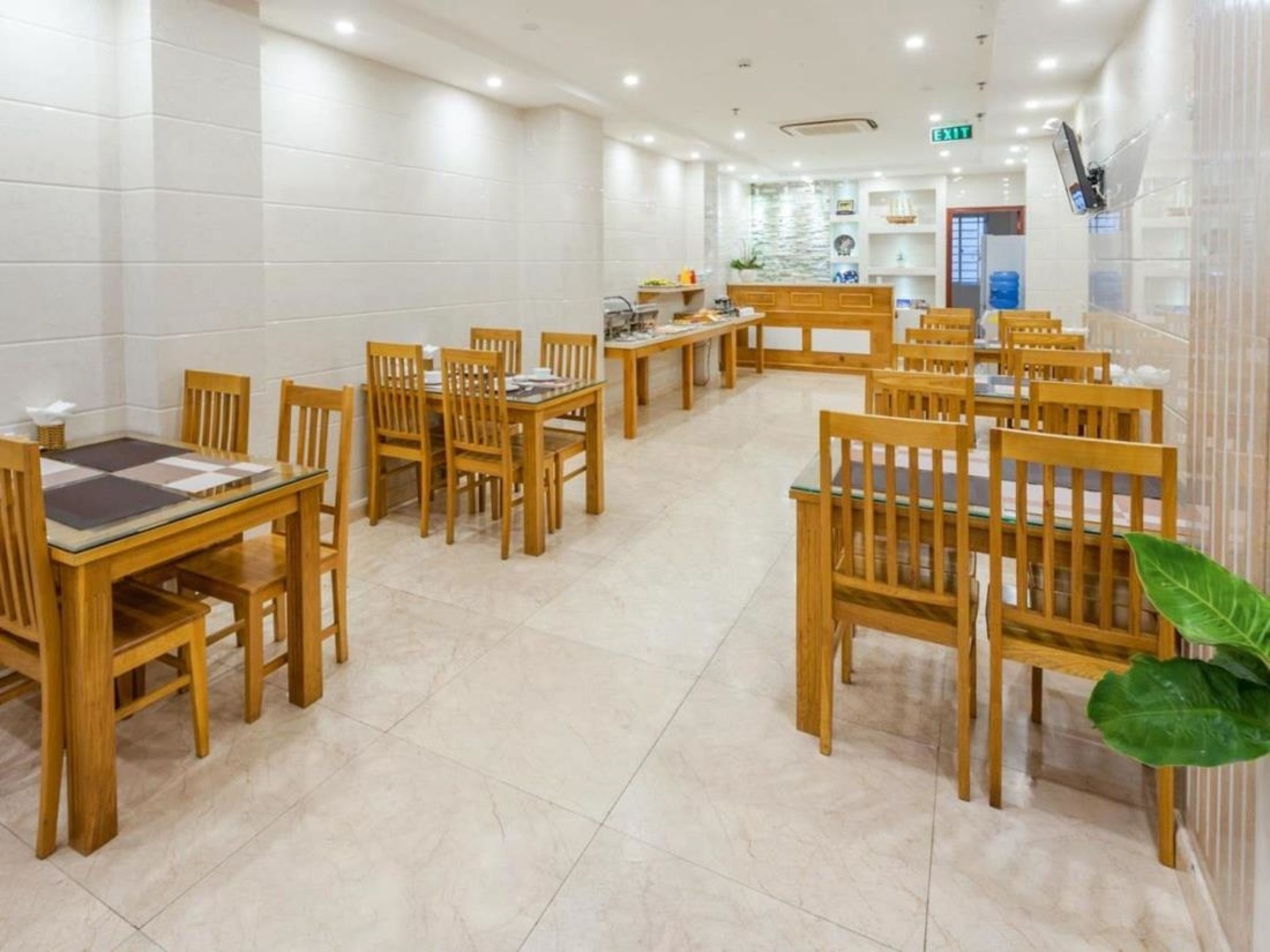 A clean, well-lit dining area with wooden tables and chairs, a tiled floor, and a visible exit sign.