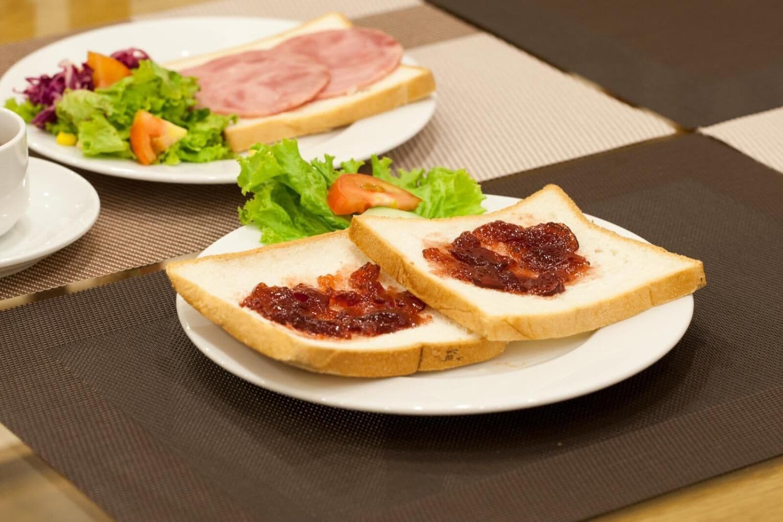 A breakfast setting with two plates of toast, one with jam and the other with ham and cheese, and a side salad.