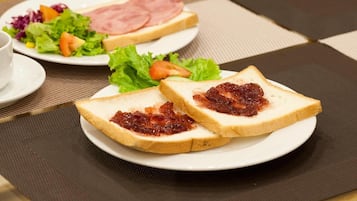 A breakfast setting with two plates of toast, one with jam and the other with ham and cheese, and a side salad.