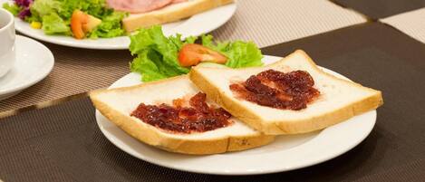 Une table mise pour le petit-déjeuner avec deux assiettes de toasts, l’une garnie de confiture et l’autre de jambon et de fromage, ainsi qu’une petite salade en accompagnement.
