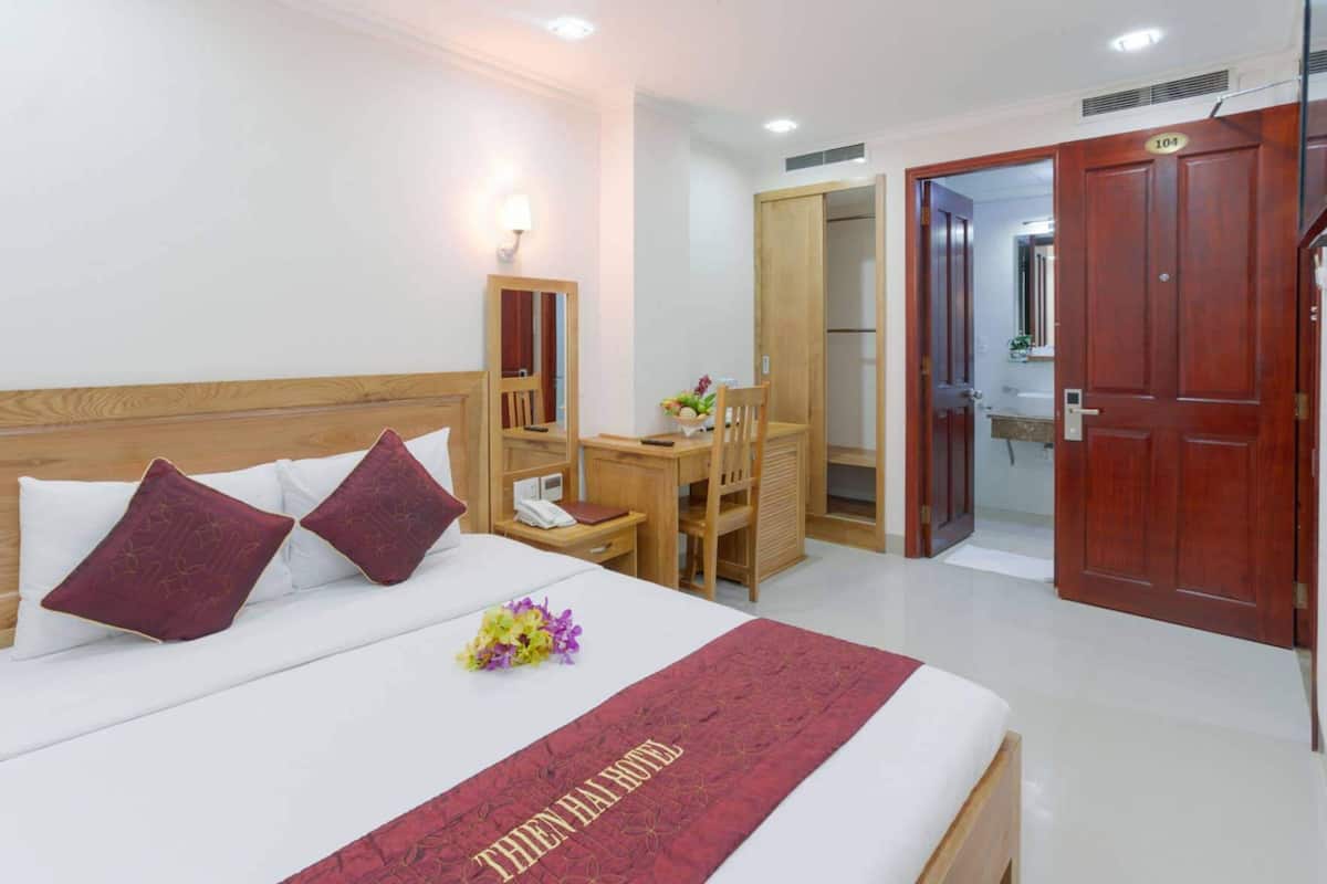 A hotel room with a bed, bedside table, chair, desk, and wardrobe.