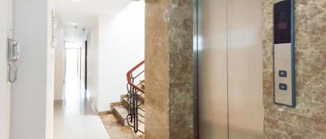 A hotel corridor with an elevator, a marble wall, a staircase, and an exit sign.