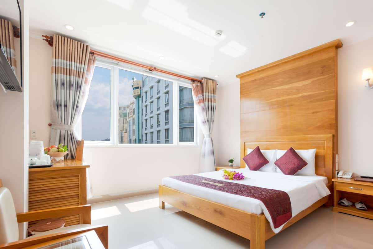 A hotel room with a large bed, wooden headboard, a desk with a telephone, and a window with curtains.