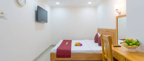 A hotel room with a bed, a desk with a chair, a television, a clock, and a fruit bowl.