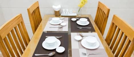 Una tavola da pranzo apparecchiata con piatti, ciotole e posate bianche, circondata da sedie di legno.