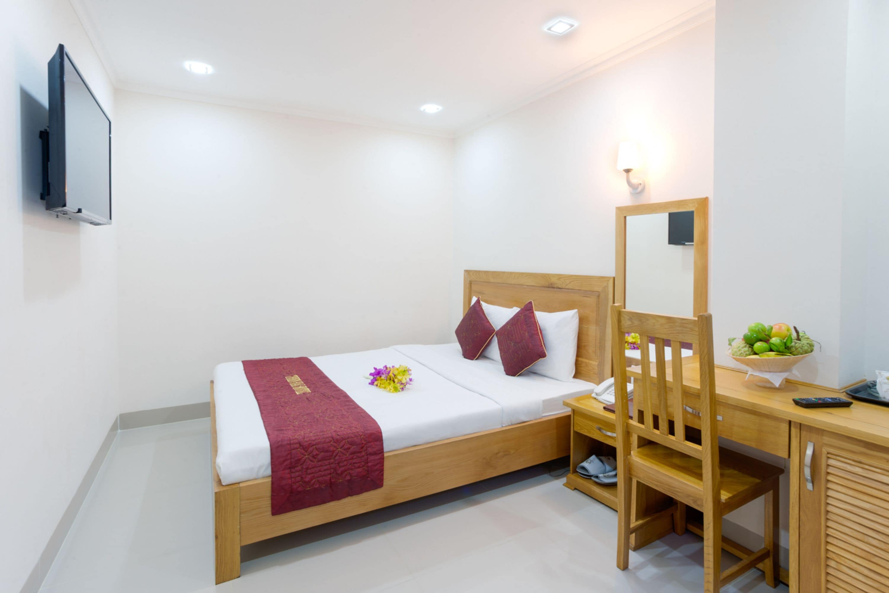 Quarto de hotel com cama, escrivaninha, cadeira, espelho e mesinha com uma tigela de frutas.