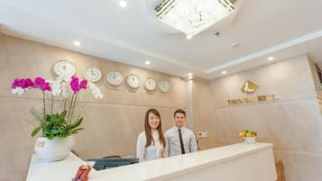 En receptionsdisk med en klocka, en växt och en skylt med texten THIEN KAI HOTEL.