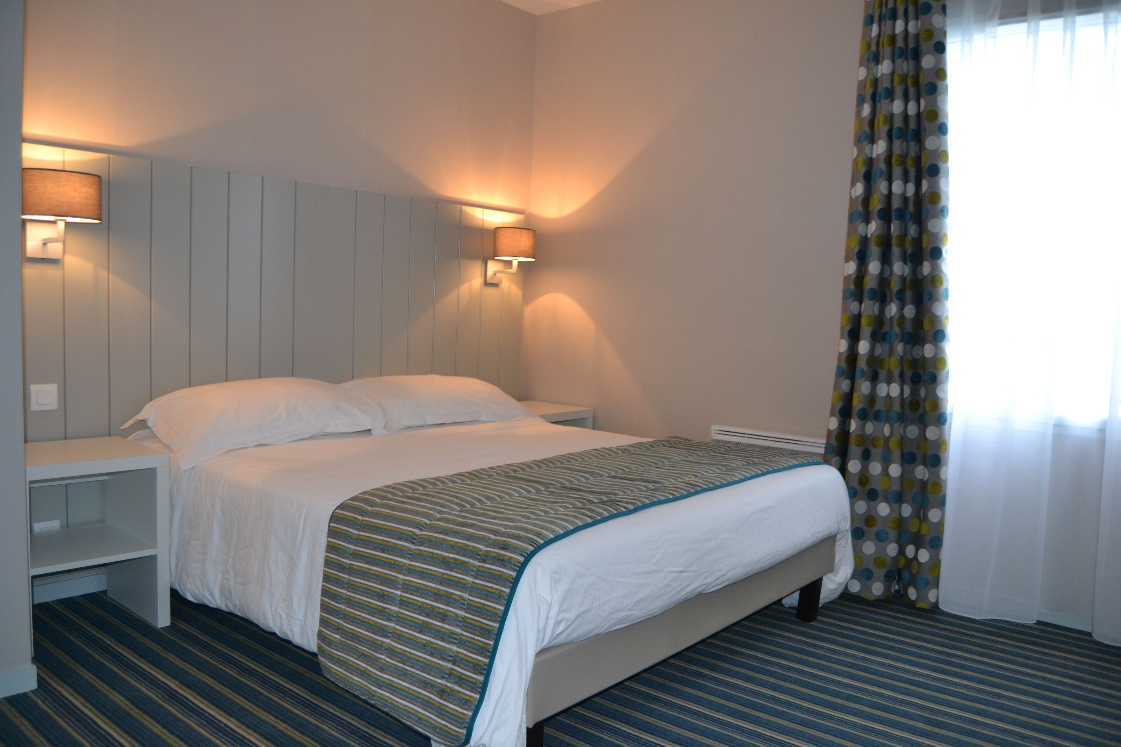 A hotel room with a bed, bedside tables, a lamp, and a window with curtains.