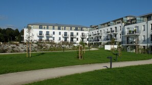 A modern multi-story residential building with balconies, a grassy courtyard, and a paved walkway.