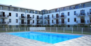 A modern apartment building with a swimming pool, balconies, and a fenced courtyard.