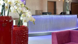 Et receptionsområde med en reception, et fjernsyn og en rød vase med hvide blomster.