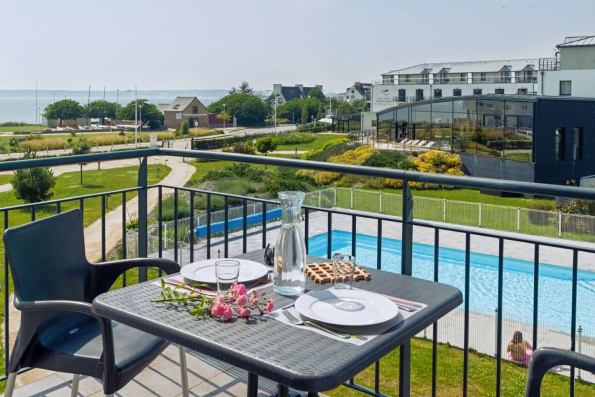 Un balcón con una mesa preparada para dos personas, con vistas a una piscina y un jardín ajardinado.