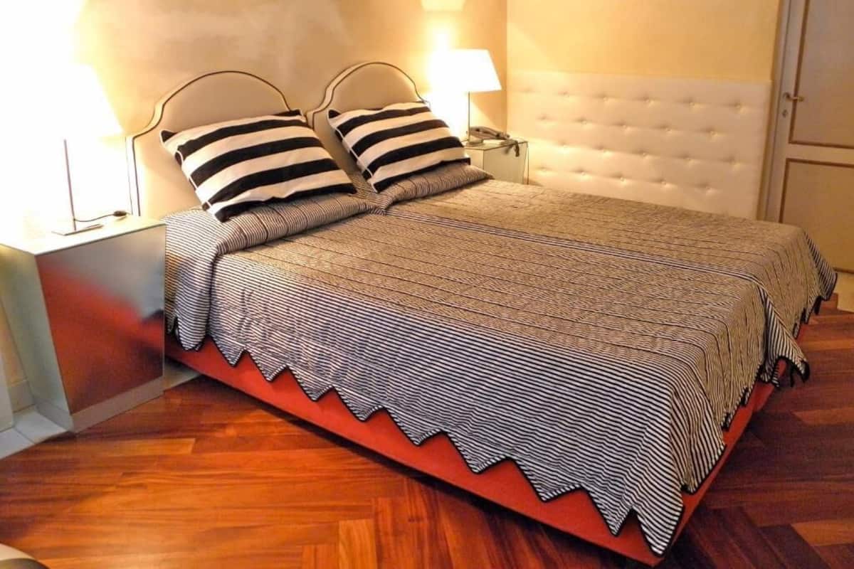 Una cama bien tendida con ropa de cama a rayas, un cabecero acolchado y lámparas de noche.