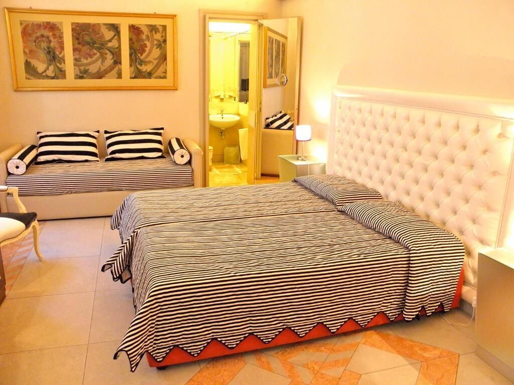 Una habitación de hotel con una cama grande, un sofá más pequeño, una mesita de noche y un espejo.