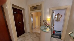 A hallway with a marble floor, a reception desk, a wooden door, and a mirror on the wall. - Residenza al Corso (Rome)