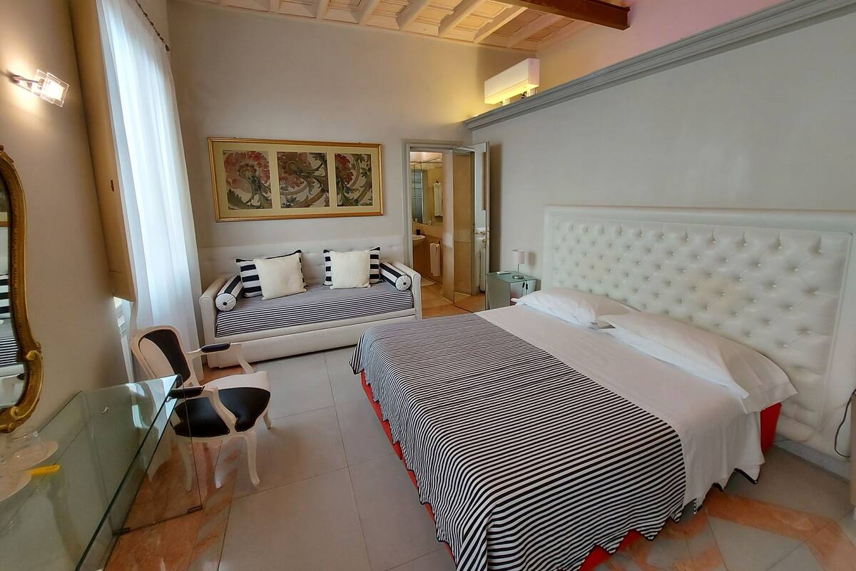 Una habitación de hotel con una cama, un sofá, una mesa de vidrio y una silla.