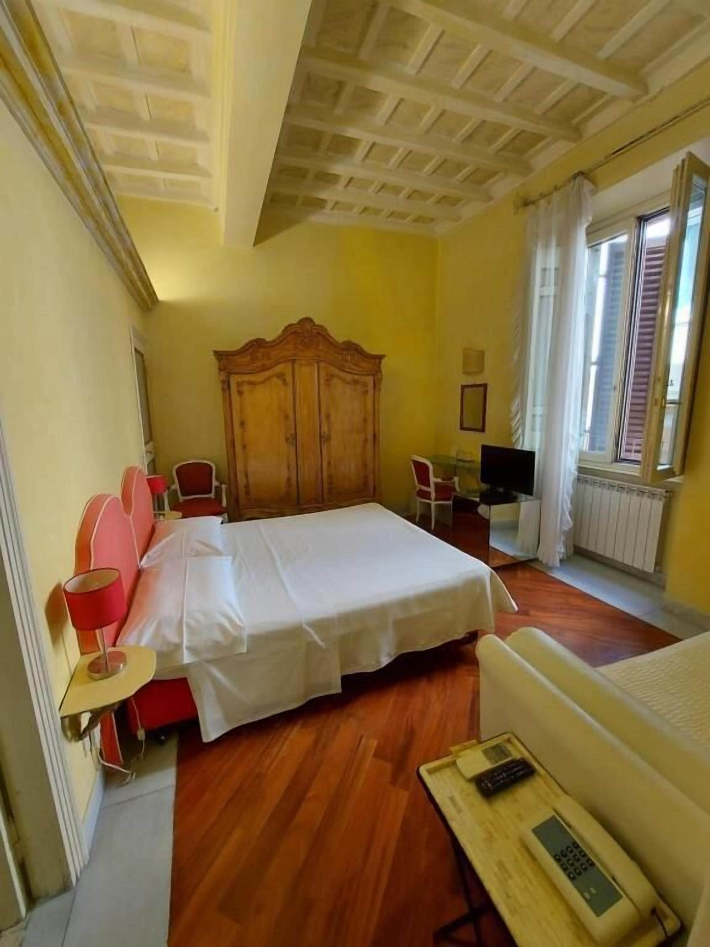 Ein Hotelzimmer mit Bett, einem Holzschrank, einem Schreibtisch mit Telefon und einem Vorhangfenster.