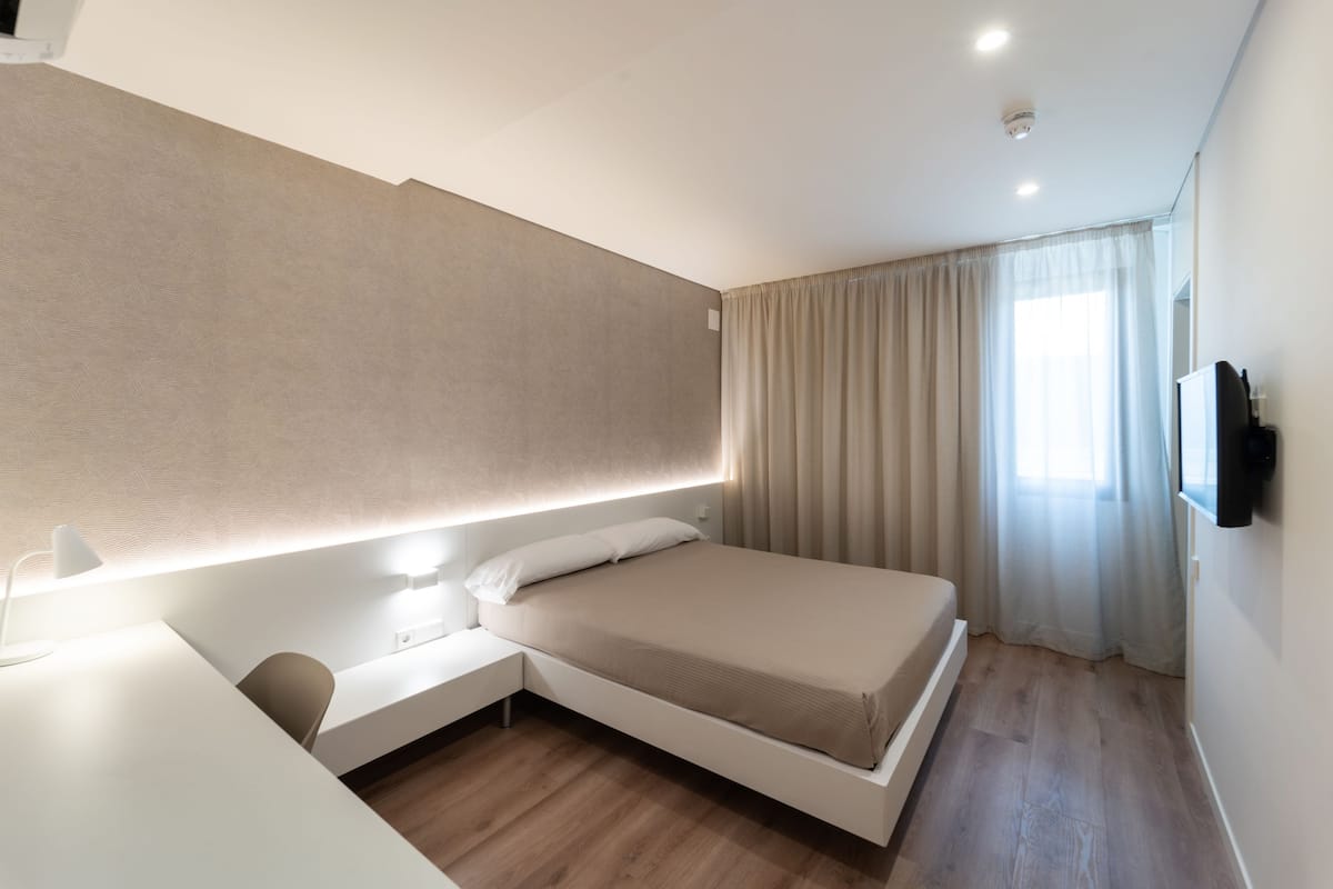 Quarto moderno com cama, mesa de cabeceira e televisão fixada na parede.