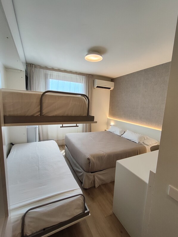 Habitación de hotel compacta con literas, un escritorio y una pequeña kitchenette.