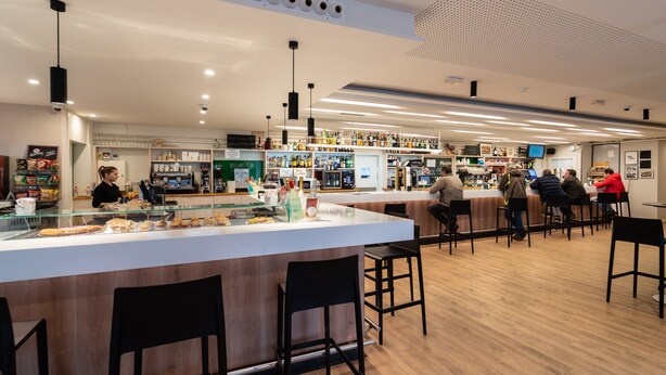 A modern bar with a long counter, black bar stools, and a variety of drinks and snacks displayed on shelves. - Hotel Las Terrazas (Burgos)