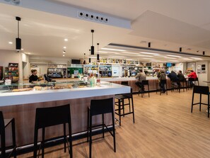 A modern bar with a long counter, black bar stools, and a variety of drinks and snacks displayed on shelves. - Hotel Las Terrazas (Burgos)