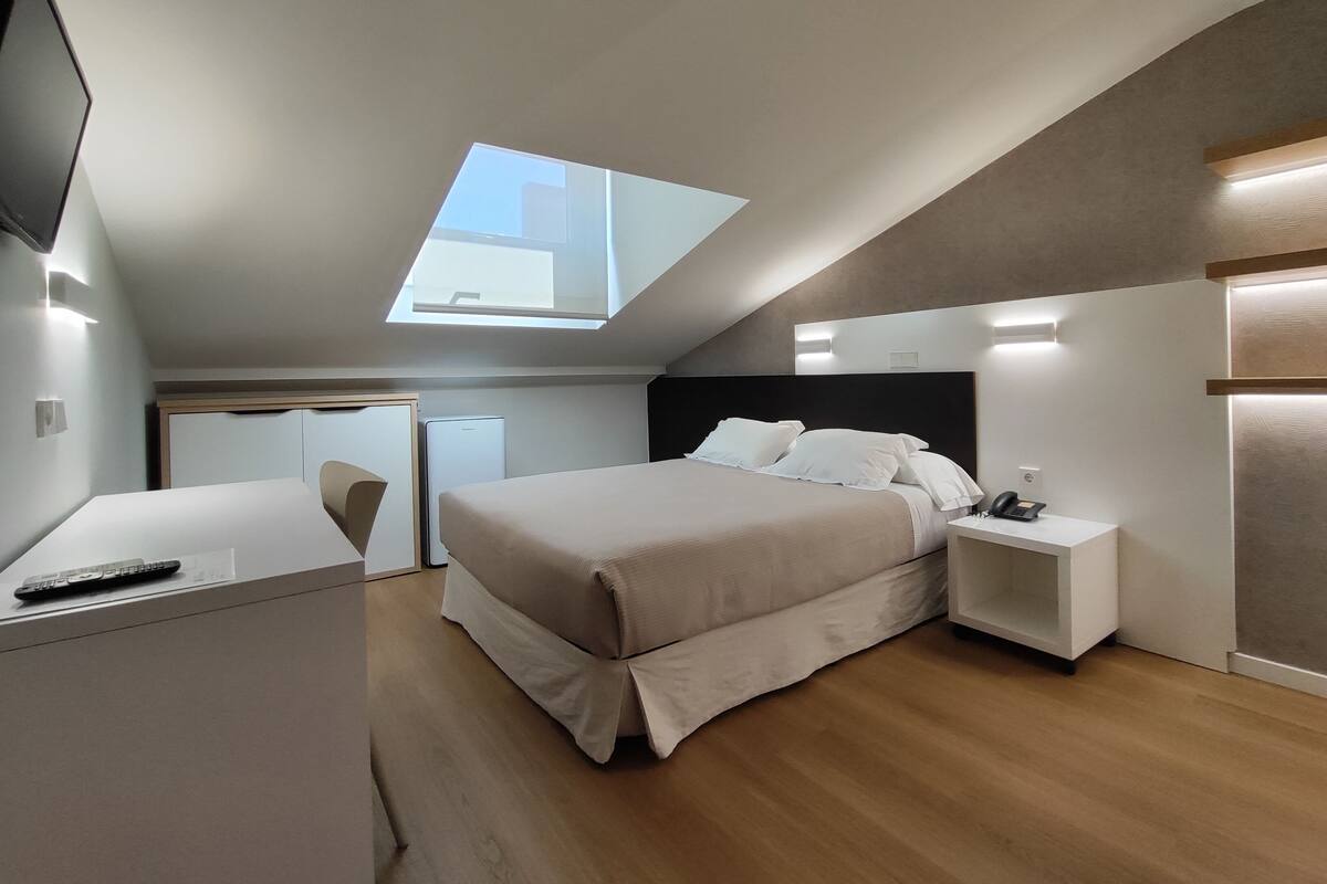 Um quarto moderno com claraboia, uma cama, mesas de cabeceira, uma escrivaninha e uma cadeira.