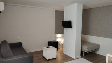 Una habitación de hotel moderna con una cama, un sofá, una mesita blanca y un televisor montado en la pared, además de una lámpara.