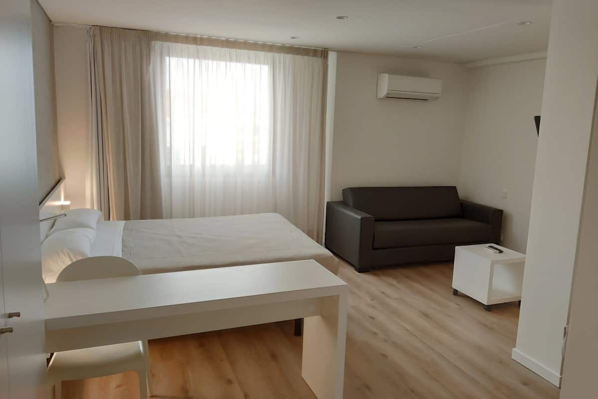 Quarto de hotel moderno com cama, escrivaninha, sofá e ar condicionado.