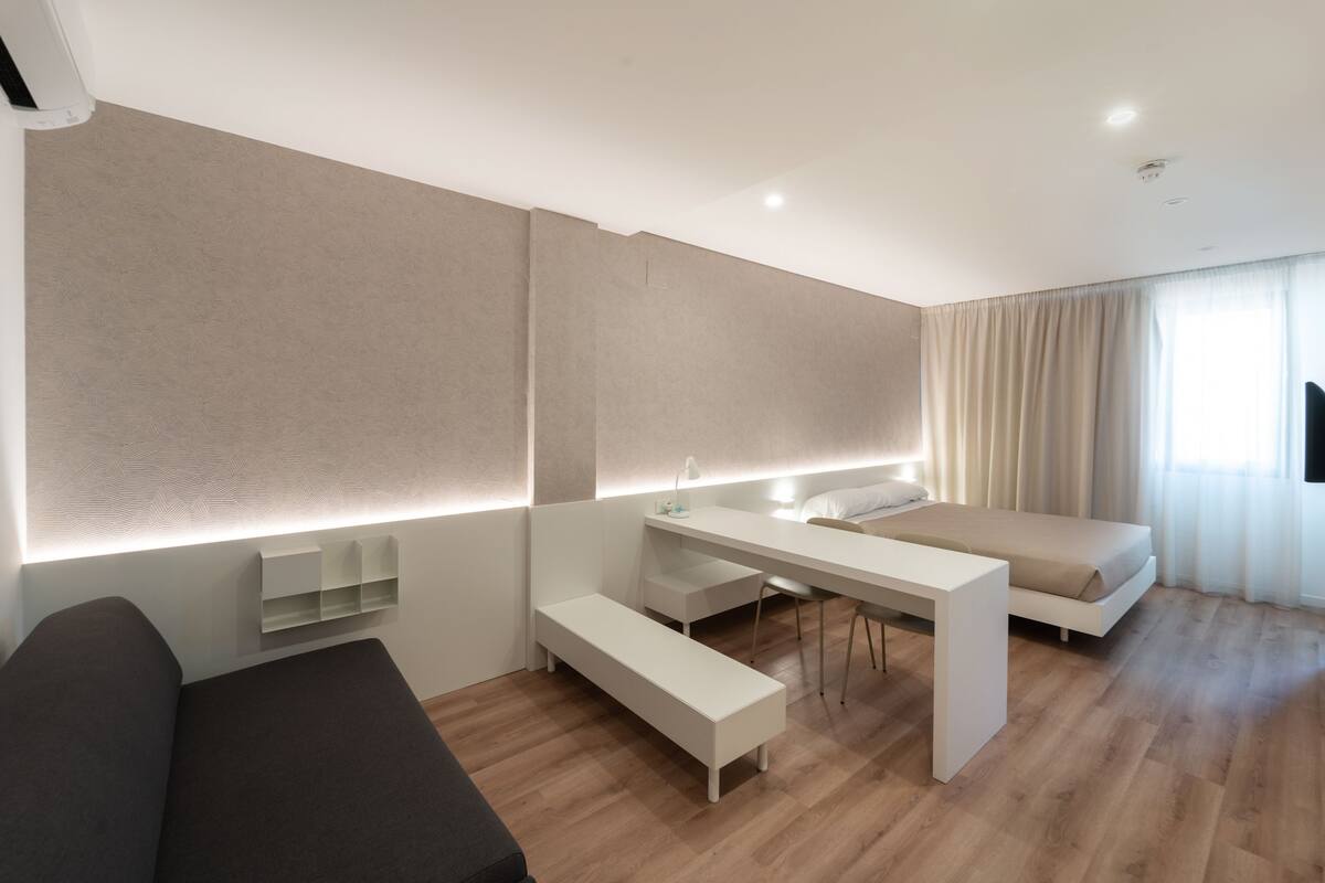 Quarto de hotel moderno com cama, escrivaninha e um banco.