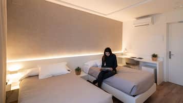 A modern hotel room with two beds, a desk, and a small plant.
