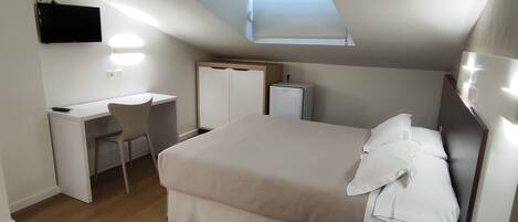 A bedroom with a skylight, a bed, a desk, and a telephone.