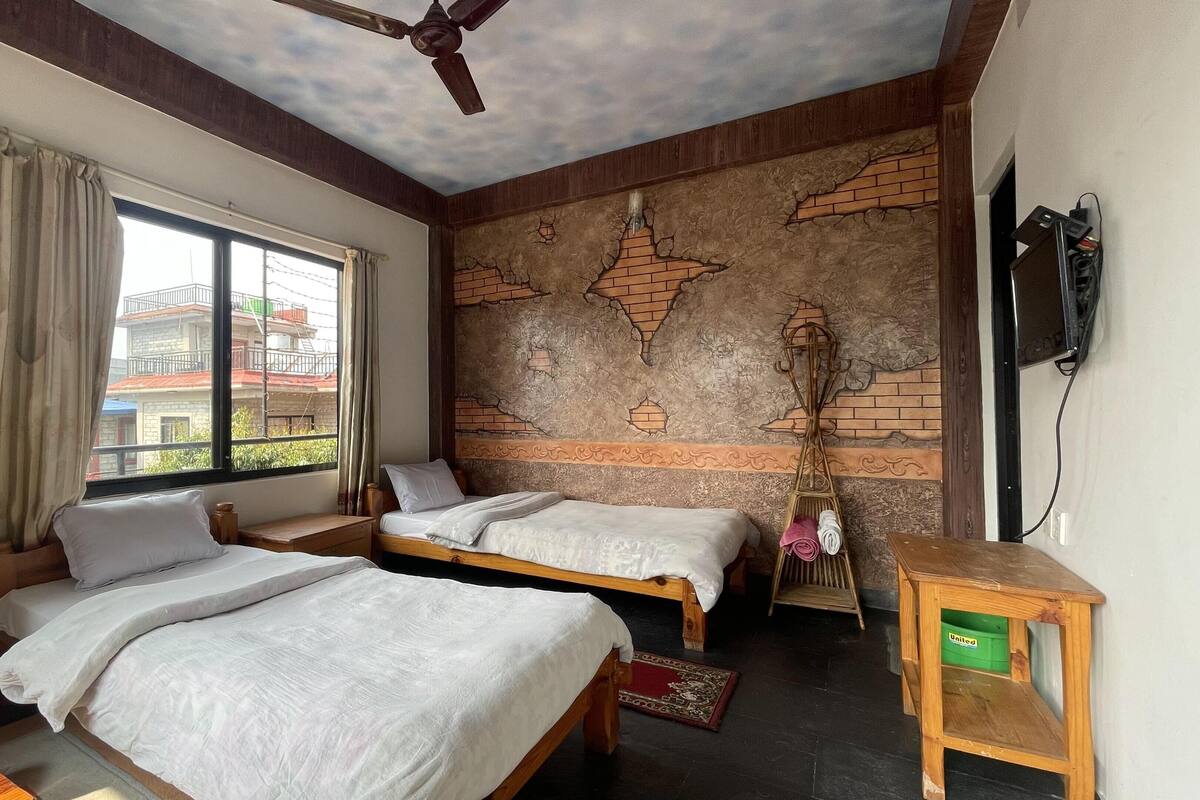 Habitación con dos camas, ventilador de techo, televisión montada en la pared y ventana con cortinas.