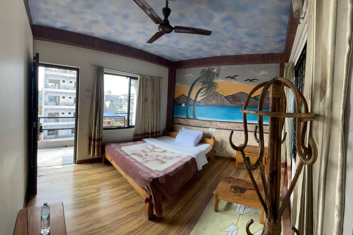 Un dormitorio con cama, ventilador de techo, un mural y vistas de edificios.