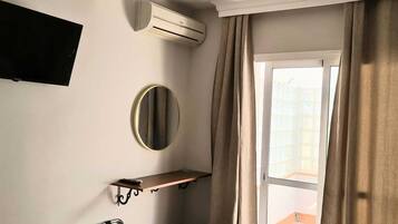 Casa de banho com espelho fixado na parede, um porta-toalhas, um prateleira e um aparelho de ar condicionado.